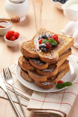 Yumurtaya, süte ve şekere batırılmış, tavada kızartılmış, beyaz tabakta taze ahududu, yaban mersini, bal, ahşap zemin üzerinde nane içeren birkaç parça ekmek.