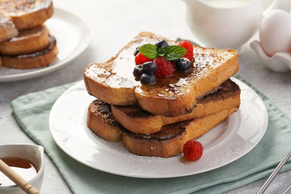 stock image Several pieces of french toast - white wheat bread soaked in egg, milk and sugar, fried on a pan - stacked on white plate with fresh raspberries, blueberries, honey, mint on light grey background