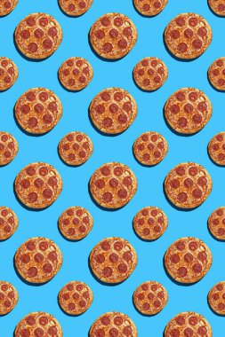 Büyük ve küçük salamlı pizza parçalarından oluşan sert bir ışık deseni pürüzsüz, parlak mavi arka plan, üst manzara, dikey