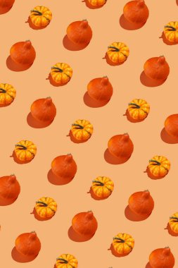 Parlak turuncu, pürüzsüz arka planda küçük sarı ve turuncu bir balkabağı deseni.,