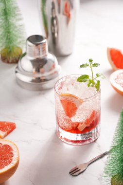 Greyfurt alkolsüz kokteyl hazırlama - Mermer yüzeyinde buz küpleri ve çelik kokteyl karıştırıcı ve bar ekipmanıyla çevrili taze naneli bardak