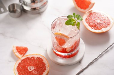 Greyfurt alkolsüz kokteyl hazırlama - Mermer yüzeyinde buz küpleri ve çelik kokteyl karıştırıcı ve bar ekipmanıyla çevrili taze naneli bardak
