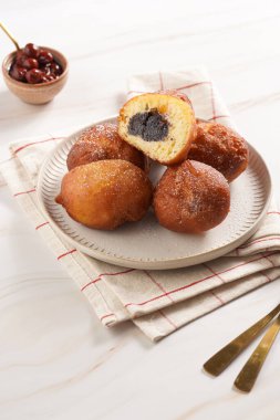 Maya hamurundan yapılmış bol yağda kızartılmış tatlı toplar. Mutfak havlusunda beyaz bir tabakta haşhaşlı ve kirazlı çörekler. Sağlıksız tatlı.