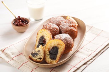 Maya hamurundan yapılmış bol yağda kızartılmış tatlı toplar. Mutfak havlusunda oval beyaz tabakta haşhaşlı ve kirazlı çörekler. Sağlıksız tatlı.