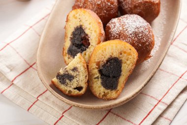 Maya hamurundan yapılmış bol yağda kızartılmış tatlı toplar. Mutfak havlusunda oval beyaz tabakta haşhaşlı ve kirazlı çörekler. Sağlıksız tatlı.