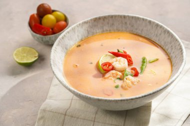 Hindistan cevizi çorbası ya da Hindistan cevizi sütü, kiraz domatesinden yapılmış köri, bezelye, biber, limon, zencefil, karides ve gri beton zeminde taze kişniş havlusu.