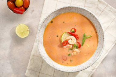 Hindistan cevizi çorbası ya da Hindistan cevizi sütü, kiraz domatesinden yapılmış köri, bezelye, biber, limon, zencefil, karides ve gri beton zeminde taze kişniş havlusu.