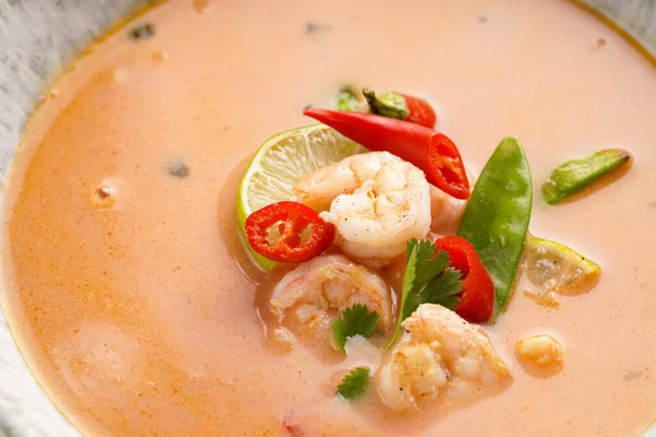 a spicy thai coconut soup or curry made of coconut milk, cherry tomatoes, snow pea, chili pepper, lime, ginger, shrimps and fresh cilantro, extreme close-up