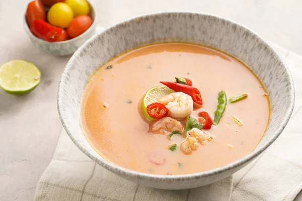 a spicy thai coconut soup or curry made of coconut milk, cherry tomatoes, snow pea, chili pepper, lime, ginger, shrimps and fresh cilantro on kitchen towel on grey concrete background