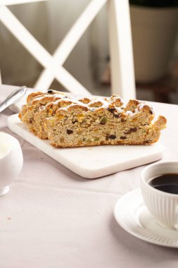 Geleneksel Alman noel pastası mermer kesim tahtasında, kahve fincanında, masa örtüsünde tereyağı tabağında ve arkada da skandal tarzı mutfak sandalyesinde.