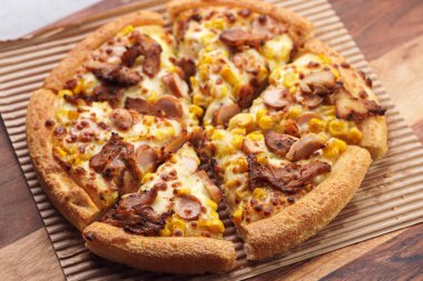 Freshly baked american pan pizza with a lot of cheese, chicken sausage, thin and crispy kebab meat and corn on a wooden board, take-away dish