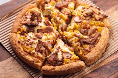 Freshly baked american pan pizza with a lot of cheese, chicken sausage, thin and crispy kebab meat and corn on a wooden board, take-away dish