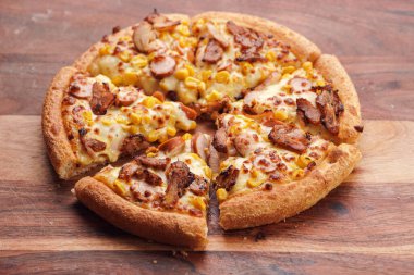 Freshly baked american pan pizza with a lot of cheese, chicken sausage, thin and crispy kebab meat and corn on a wooden board, take-away dish