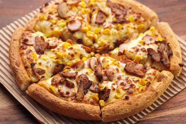 Freshly baked american pan pizza with a lot of cheese, chicken sausage, thin and crispy kebab meat and corn on a wooden board, take-away dish