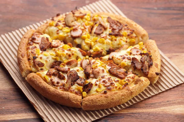 Freshly baked american pan pizza with a lot of cheese, chicken sausage, thin and crispy kebab meat and corn on a wooden board, take-away dish