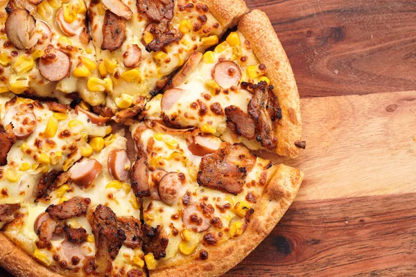 Freshly baked american pan pizza with a lot of cheese, chicken sausage, thin and crispy kebab meat and corn on a wooden board, take-away dish, top view