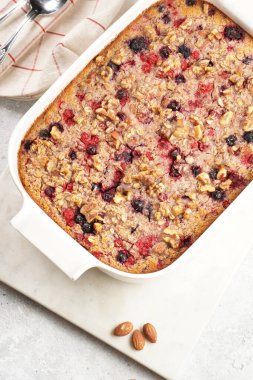 breakfast casserole idea - oven berry baked oatmeal with almonds, walnuts and coconut flakes in a white porcelain baking form on a marble board, top view