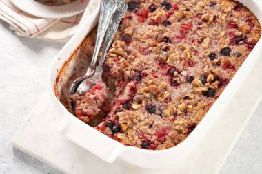 breakfast casserole idea - oven berry baked oatmeal with almonds, walnuts and coconut flakes in a white porcelain baking form on a marble board, top view