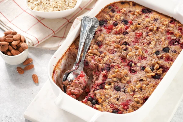 breakfast casserole idea - oven berry baked oatmeal with almonds, walnuts and coconut flakes in a white porcelain baking form on a marble board, top view