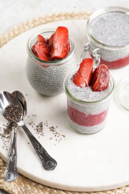 Breakfast idea - glass mason jars with chia seeds pudding, frozen strawberries and red raspberry smoothie on round marble board