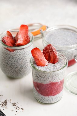 Breakfast idea - glass mason jars with chia seeds pudding, frozen strawberries and red raspberry smoothie on round marble board