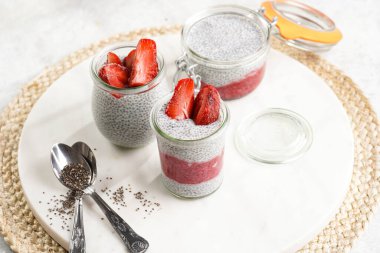 Breakfast idea - glass mason jars with chia seeds pudding, frozen strawberries and red raspberry smoothie on round marble board