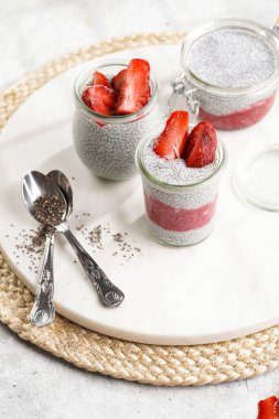 Breakfast idea - glass mason jars with chia seeds pudding, frozen strawberries and red raspberry smoothie on round marble board with easter decoration: spring branch of willow