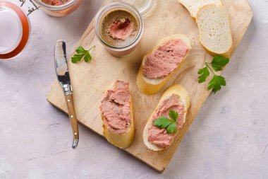 Homemade chicken liver pate on fresh french white wheat baguette slices on wooden board, glass mason jars with cooked liverwurst, top view