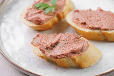 Homemade chicken liver pate on fresh french white wheat baguette slices on ceramic plate, glass mason jars with cooked liverwurst