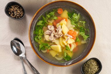 Patates, havuç, kereviz, bej renkli mutfak masası örtüsü üzerinde taze maydanoz ve geleneksel Avrupa tavuk çorbası içeren iki derin yeşil kase.