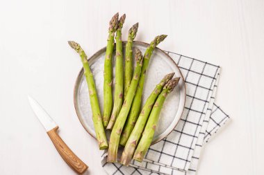 Beyaz ahşap bir arka planda, skandal tarzı bir tabakta taze, çiğ kuşkonmaz.