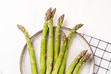 Beyaz ahşap bir arka planda, skandal tarzı bir tabakta taze, çiğ kuşkonmaz.