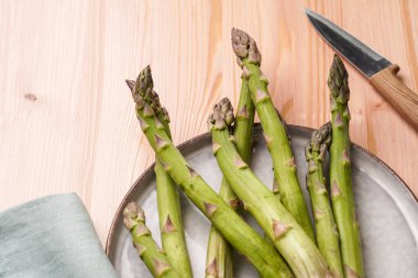 Bir demet taze çiğ kuşkonmaz, ahşap bir arka planda, skandal stili bir tabakta.