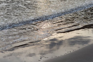 Akdeniz 'in akşam kumsalındaki dalgalar, güneşin sudaki yansıması.
