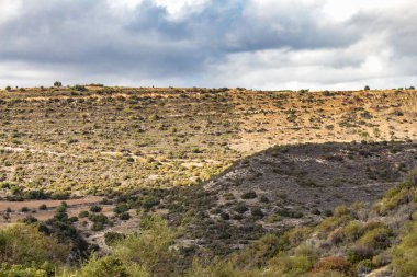 Kıbrıs Rum Kesimi 'nin berrak gökyüzü, az bulut ve sınırlı bitki örtüsü ile manzaralı sakin bir fotoğraf, adanın doğal güzelliğini gösteriyor