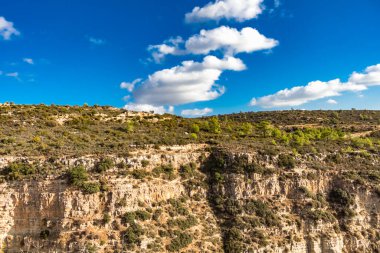 Kıbrıs dağlarında seyrek çalılıklara sahip tenha bir kaya oluşumu, dağlık bölgenin sakinliğini ve doğal güzelliğini yansıtıyor.