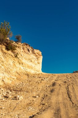 Mavi gökyüzü ve solunda küçük bir uçurum bulunan yükselen toprak yolun göz kamaştırıcı manzarası, Kıbrıs 'ın dağlık arazisinde