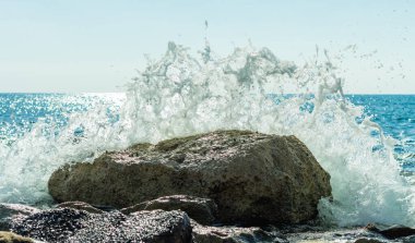 Bir Kıbrıs plajında kayalara çarpan deniz dalgalarının fotoğrafı, su sıçramaları, okyanus gelgitlerinin gücü ve güzelliğini yansıtıyor.