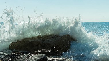 Bir Kıbrıs plajında kayalara çarpan deniz dalgalarının fotoğrafı, su sıçramaları, okyanus gelgitlerinin gücü ve güzelliğini yansıtıyor.