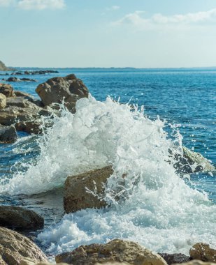 Bir Kıbrıs plajında kayalara çarpan deniz dalgalarının fotoğrafı, su sıçramaları, okyanus gelgitlerinin gücü ve güzelliğini yansıtıyor.