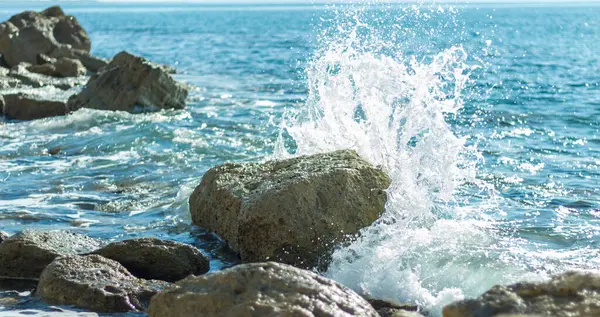 Bir Kıbrıs plajında kayalara çarpan deniz dalgalarının fotoğrafı, su sıçramaları, okyanus gelgitlerinin gücü ve güzelliğini yansıtıyor.