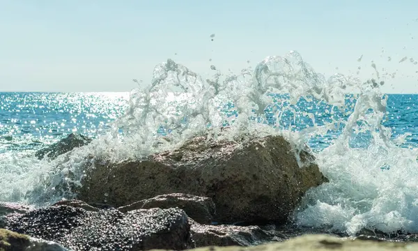 Bir Kıbrıs plajında kayalara çarpan deniz dalgalarının fotoğrafı, su sıçramaları, okyanus gelgitlerinin gücü ve güzelliğini yansıtıyor.