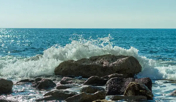 Bir Kıbrıs plajında kayalara çarpan deniz dalgalarının fotoğrafı, su sıçramaları, okyanus gelgitlerinin gücü ve güzelliğini yansıtıyor.