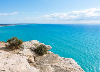Güneşli bir günde Kıbrıs 'taki bir uçurumdan Akdeniz' in nefes kesen manzarasına hayret ediyorum. Ufuk, denizin engin genişliğine sonsuz bir şekilde uzanıyor. Huzurlu ve büyüleyici bir manzara yaratıyor.