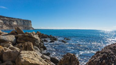 Kıbrıs 'taki Zapallo Körfezi Sahili' nin güzelliğini yaşayın kumlu kıyıları, denize dağılmış kayalar, güneşli bir günün sıcacık kucağında beyaz bir uçurum.