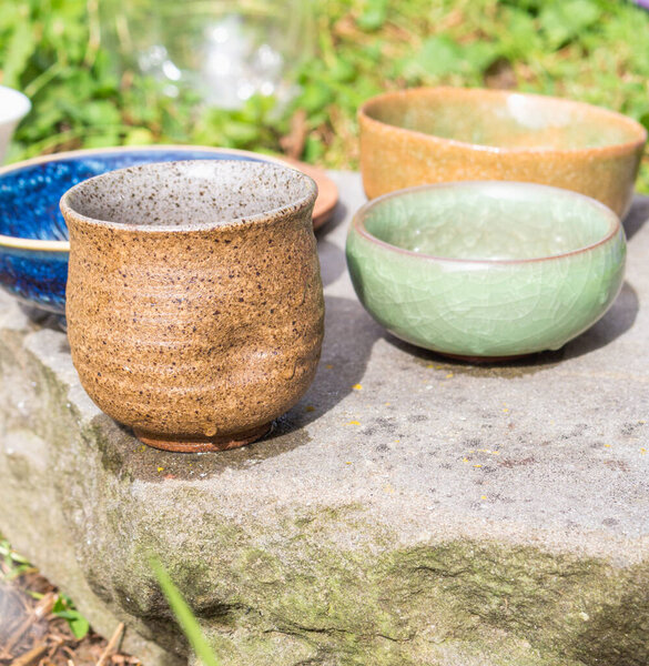 Погрузитесь в элегантность чайной церемонии с глиняными чашами, сосудом чая, камнем, цветочными украшениями и пышной зеленой травой, создавая спокойную и гармоничную атмосферу