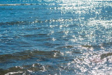 Güneşli suyun dingin güzelliğini yansıtan bir görüntü. Güneş ışığının dalgalanan yüzeyindeki yansımalarıyla oluşan ışıltılı bir efekt.