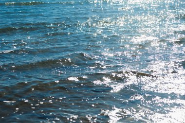 Güneşli suyun dingin güzelliğini yansıtan bir görüntü. Güneş ışığının dalgalanan yüzeyindeki yansımalarıyla oluşan ışıltılı bir efekt.