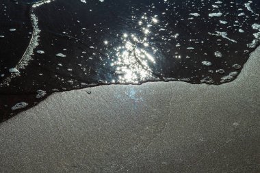 Büyüleyici bir siyah beyaz fotoğraf güçlü bir dalganın sahile çarptığı anı yakalıyor. Karanlık dalga ve aydınlık kum arasındaki zıtlık dramatik bir sahne yaratır.