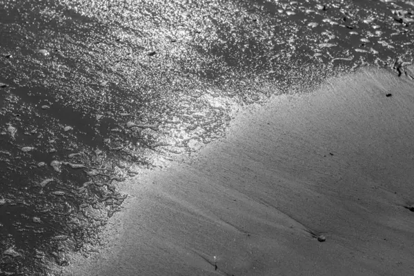 Büyüleyici bir siyah beyaz fotoğraf güçlü bir dalganın sahile çarptığı anı yakalıyor. Karanlık dalga ve aydınlık kum arasındaki zıtlık dramatik bir sahne yaratır.